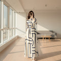 Person wearing a white dress with blue geometric patterns, standing in a room with abstract art on the wall.